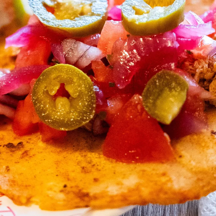 Close-up van een soft taco met pulled chicken, tomaat, rode ui en jalapeno
